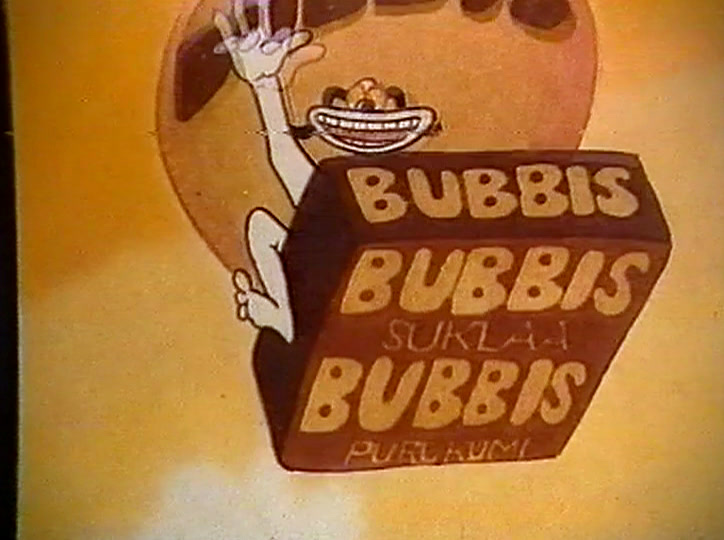 Hän pitää ylhäällä ruskeaa pakettia, jossa lukee BUBBIS SUKLAA BUBBIS PURUKUMI.