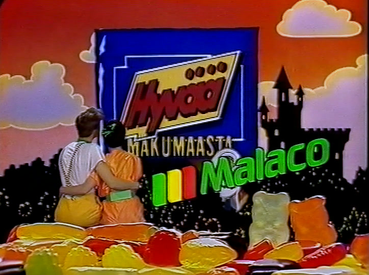 Kaksi lasta istuu käsikkäin hyytelökarkkikasan päällä, vieressä Malaco-logo.