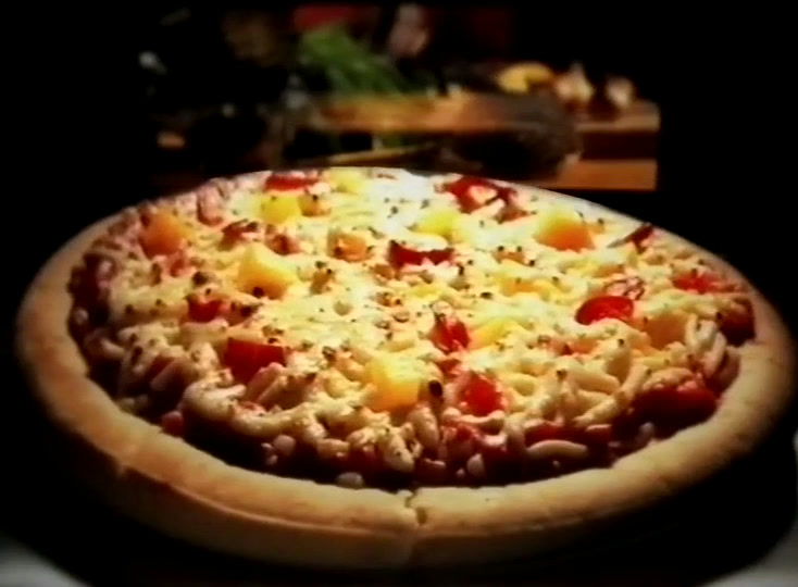 Paistettu pizza tummalla tasolla, ruskistunutta juustoa sekä keltaisia ja punaisia paloja