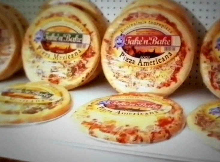Kelmutettuja tuoreita pizzoja valkoisella hyllyllä, etiketeissä lukee Take’n’Bake Pizza Americana ja Mexicana