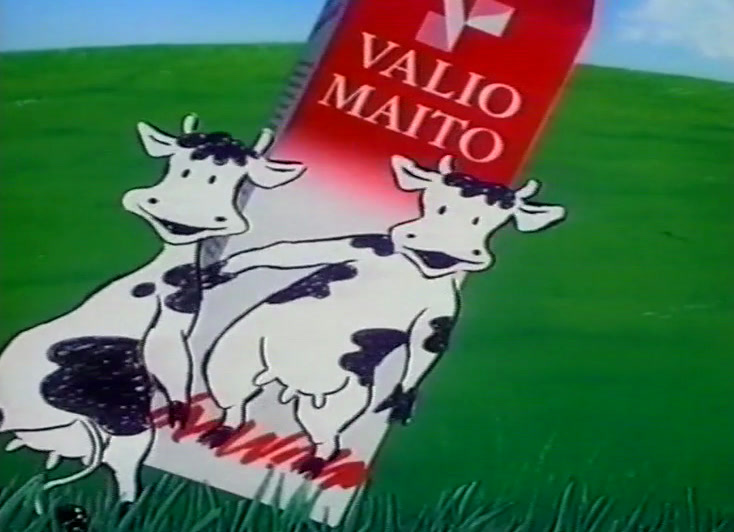Punainen tölkki seisoo ruohikossa, yksi lehmä katsoo ylös ja toinen tanssii sorkat koholla.