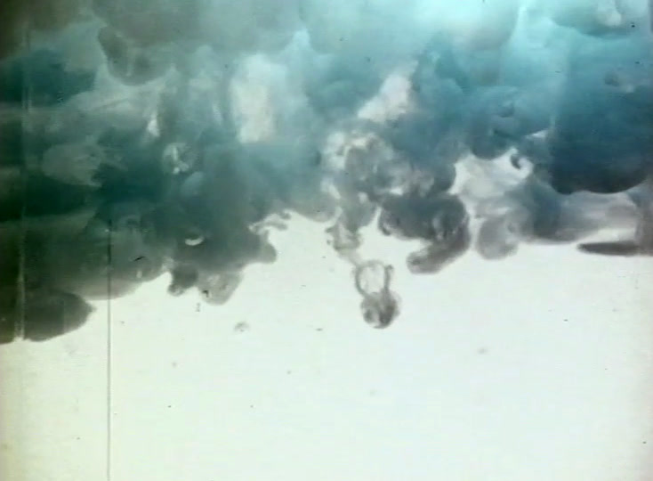 Dark blue-green ink billows through pale water, filmed close, filling the top of the frame.