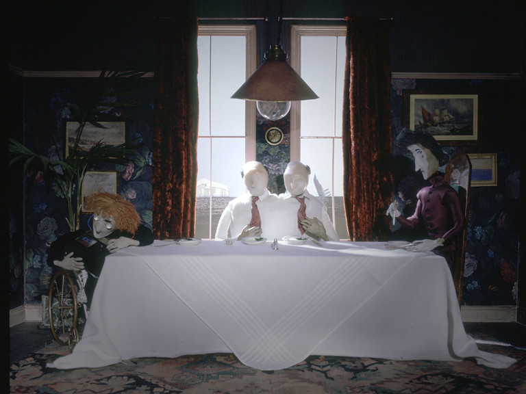 Still from The Stain, puppet figures around a dining table